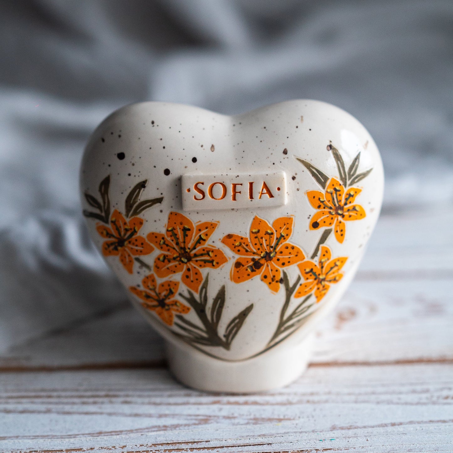 Hand-painted heart-shaped ceramic urn with vibrant orange lilies and a matching stand for human or pet ashes.