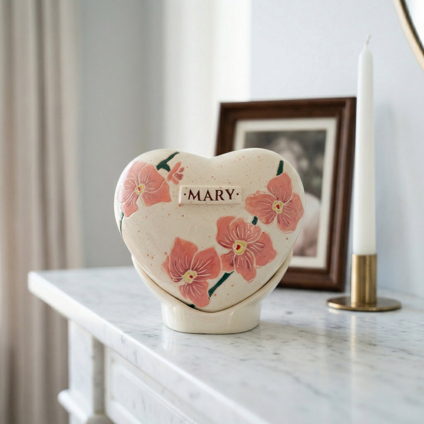 A sophisticated home memorial display with an orchid flower heart urn on a marble shelf next to a small candle.