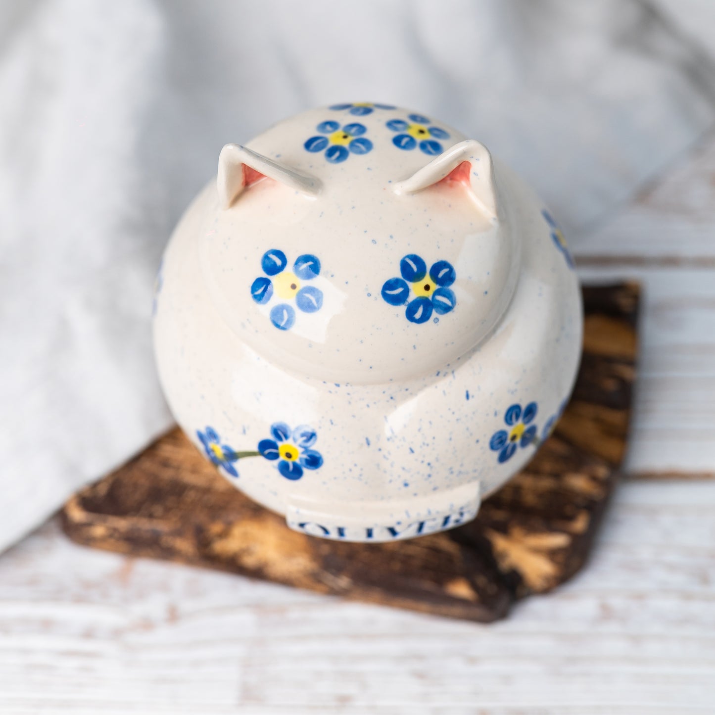 Overhead view of the closed forget-me-not cat urn showing the sculpted ceramic ears and folk-art handle on the lid.