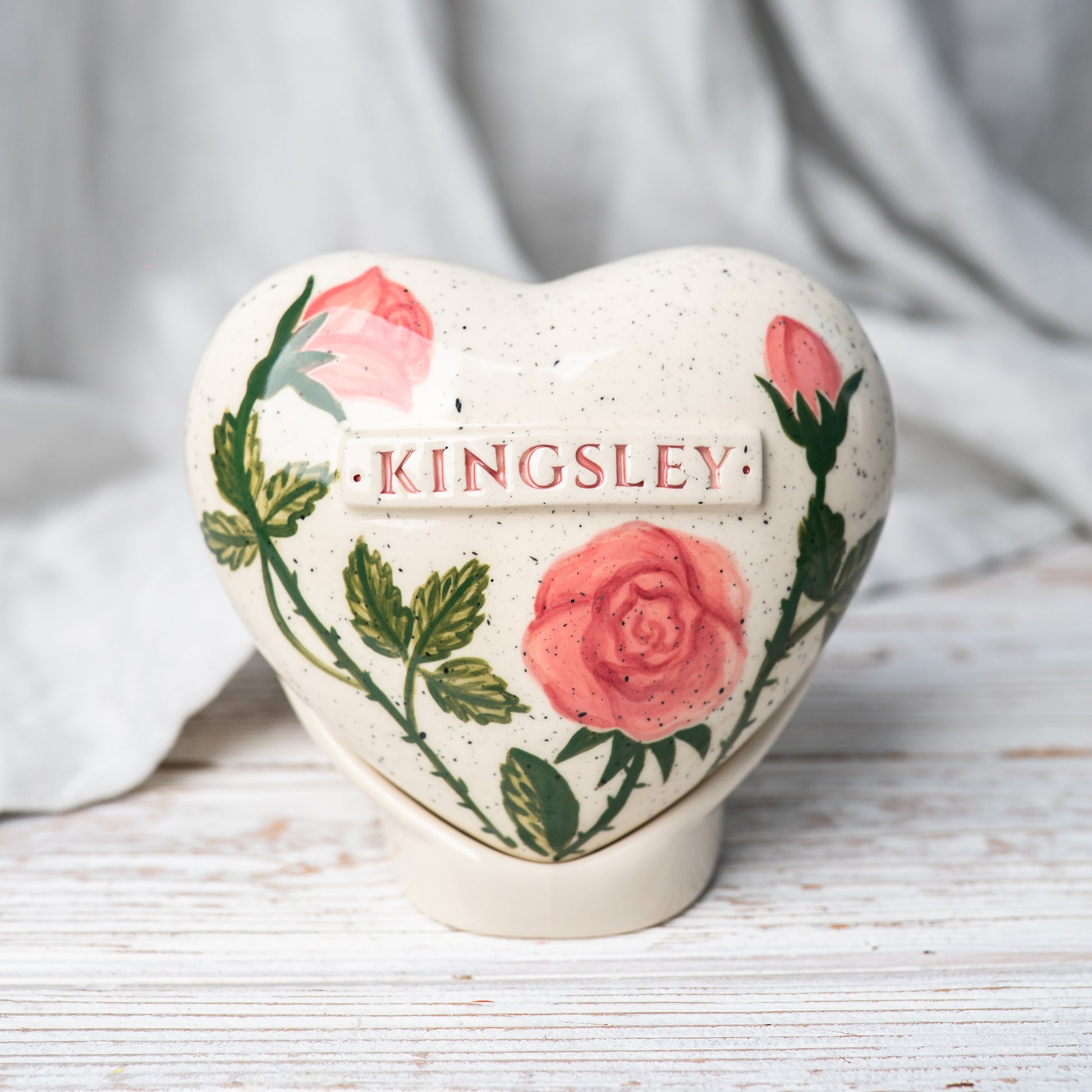 Hand-painted heart-shaped ceramic urn with elegant pink roses and a matching stand for human or pet ashes.