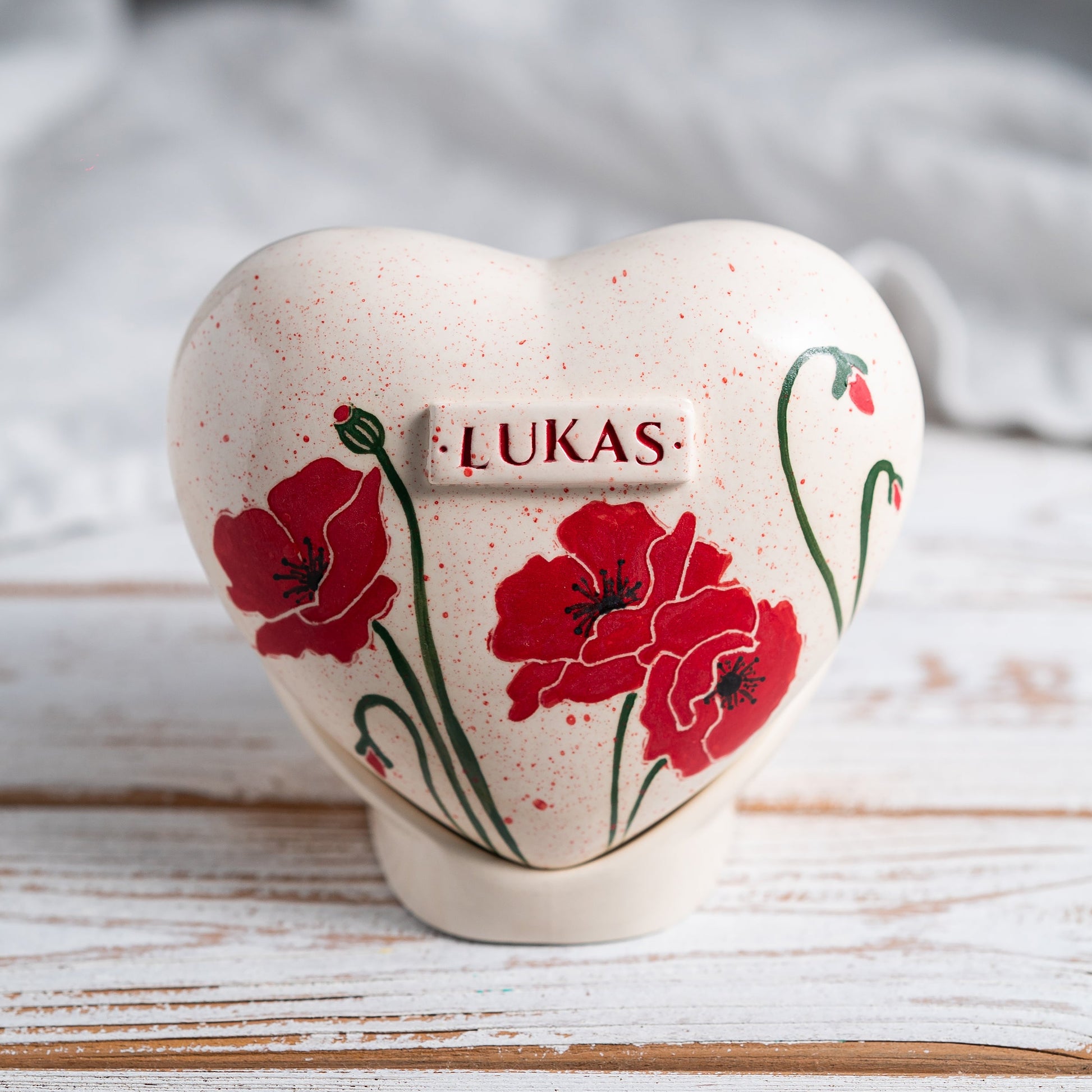 Hand-painted heart-shaped ceramic urn with vibrant red poppies and a matching stand for human or pet ashes.