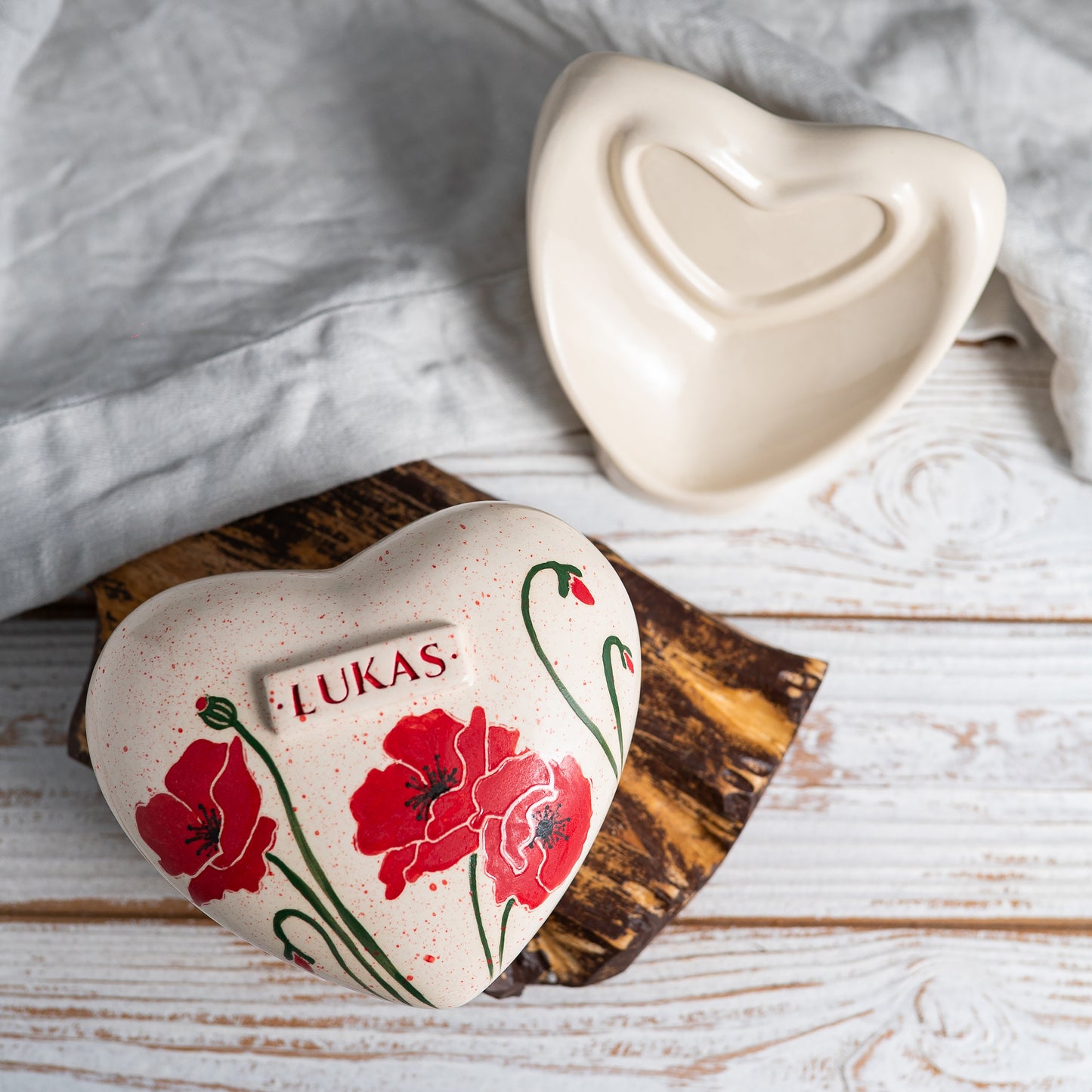 Top view of the heart-shaped ceramic urn, showing the detailed red petals and dark centers of the poppy illustration.