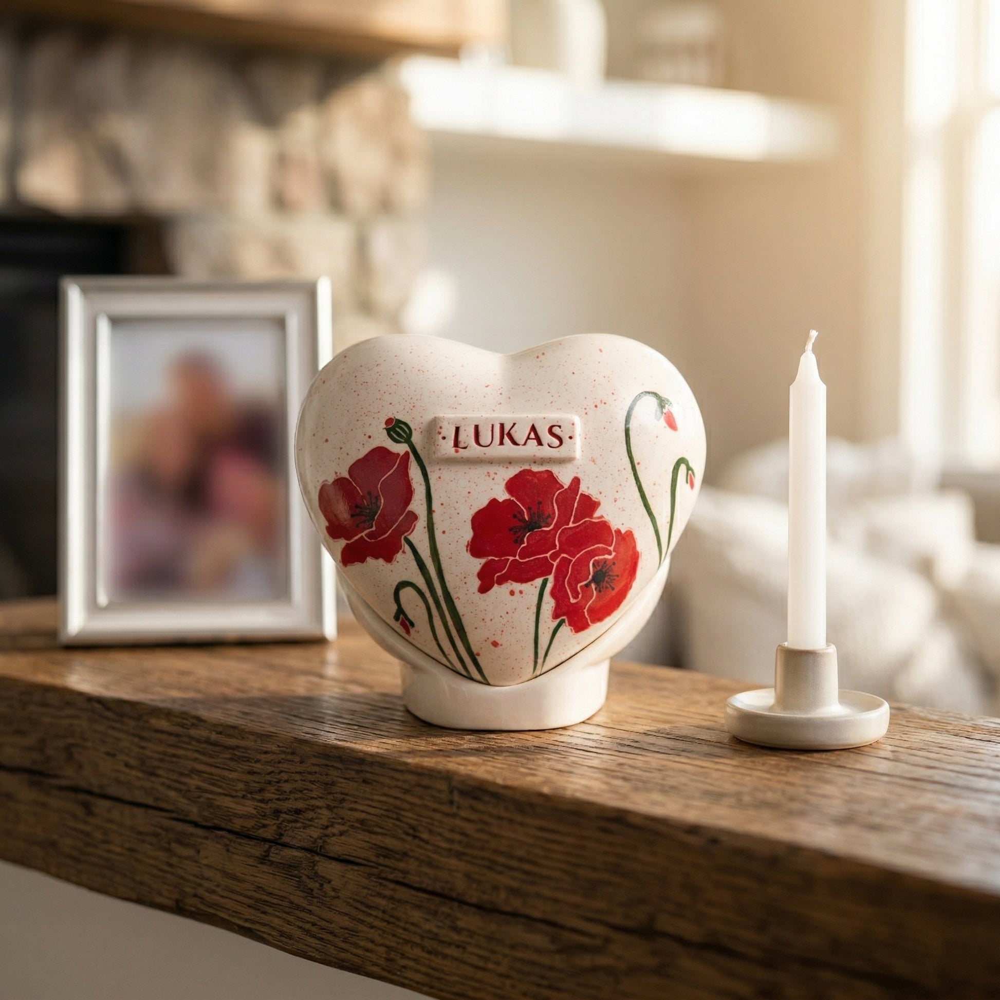 A dignified home memorial display with a red poppy flower heart urn on a wooden shelf next to a small candle.