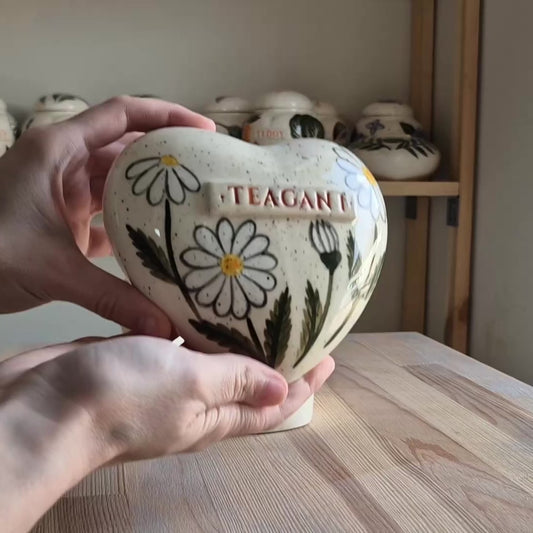 Video showcase of a hand-painted daisy heart-shaped ceramic urn on a stand