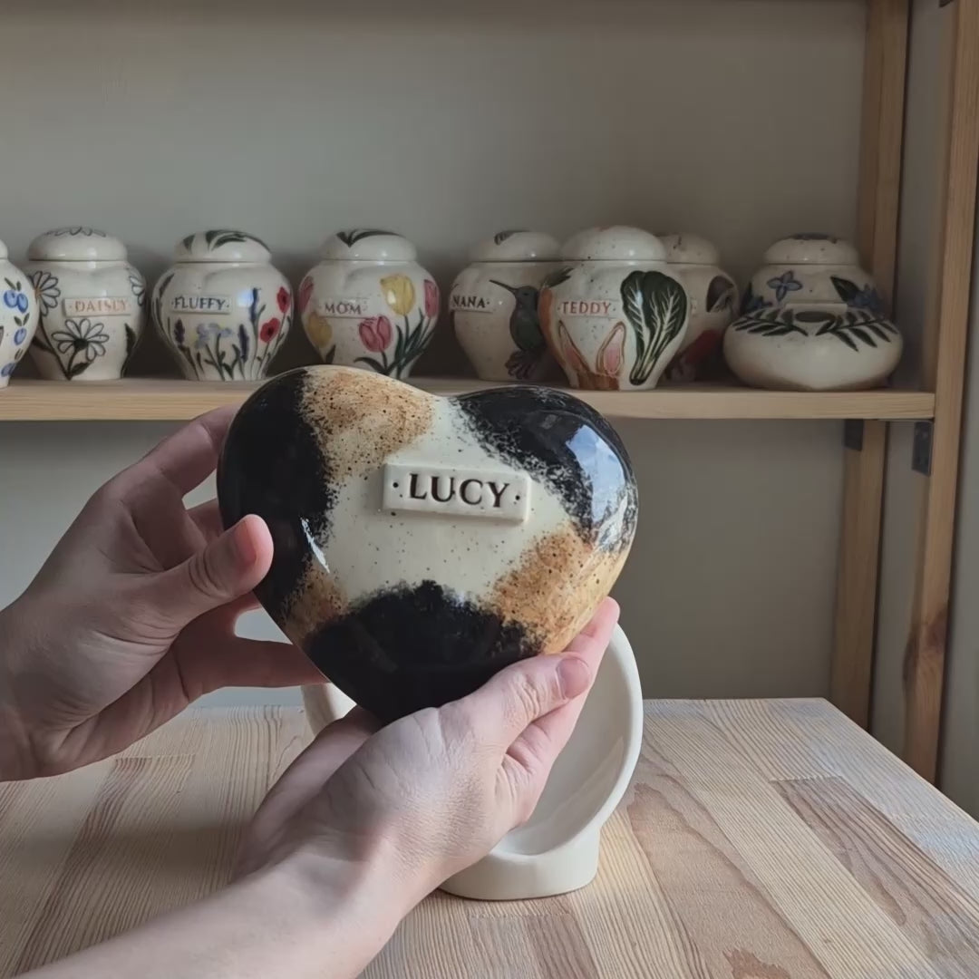 Video showcase of a hand-painted calico cat heart-shaped ceramic urn on a stand