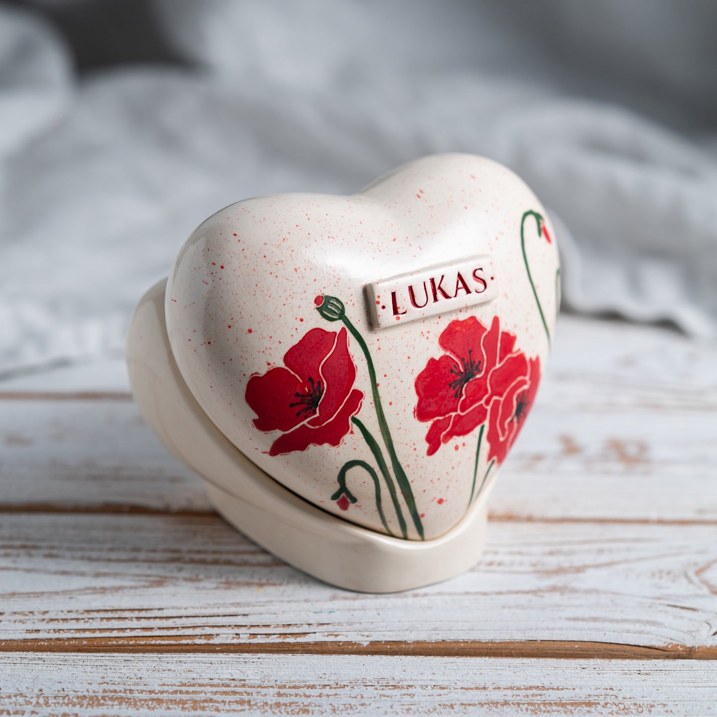 Side profile of the poppy memorial urn on its stand, highlighting the smooth glaze and handmade quality.