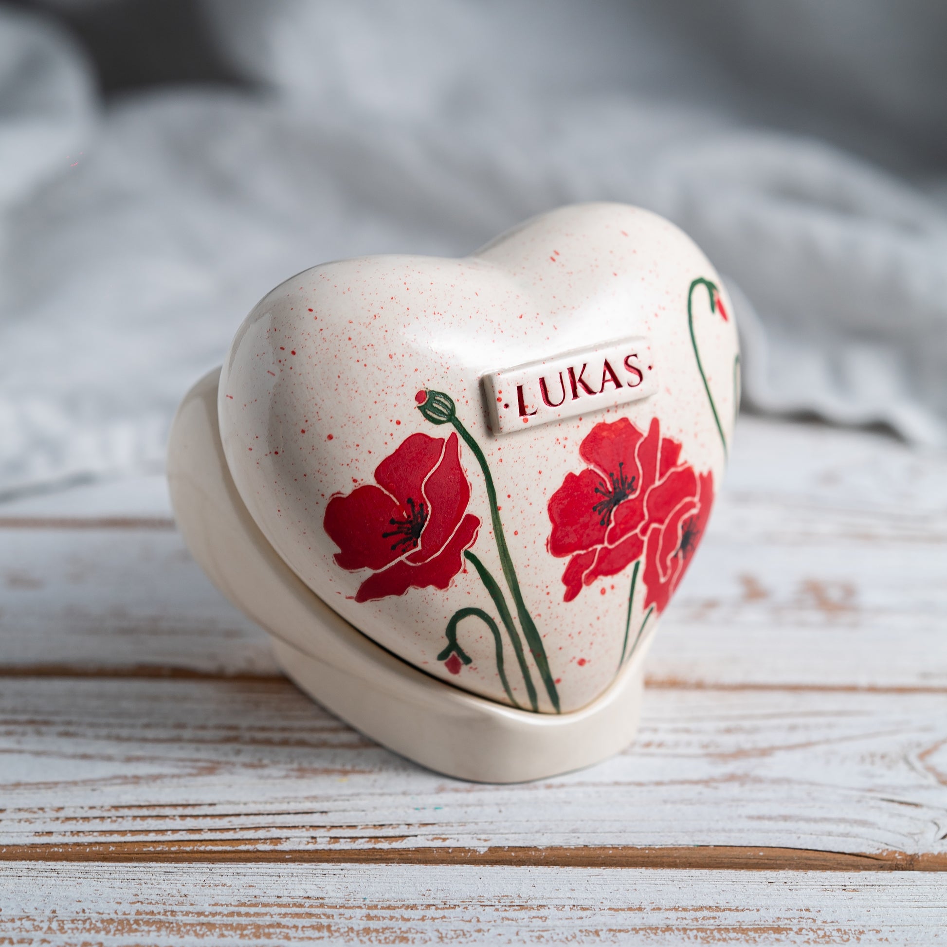 Side profile of the poppy memorial urn on its stand, highlighting the smooth glaze and handmade quality.