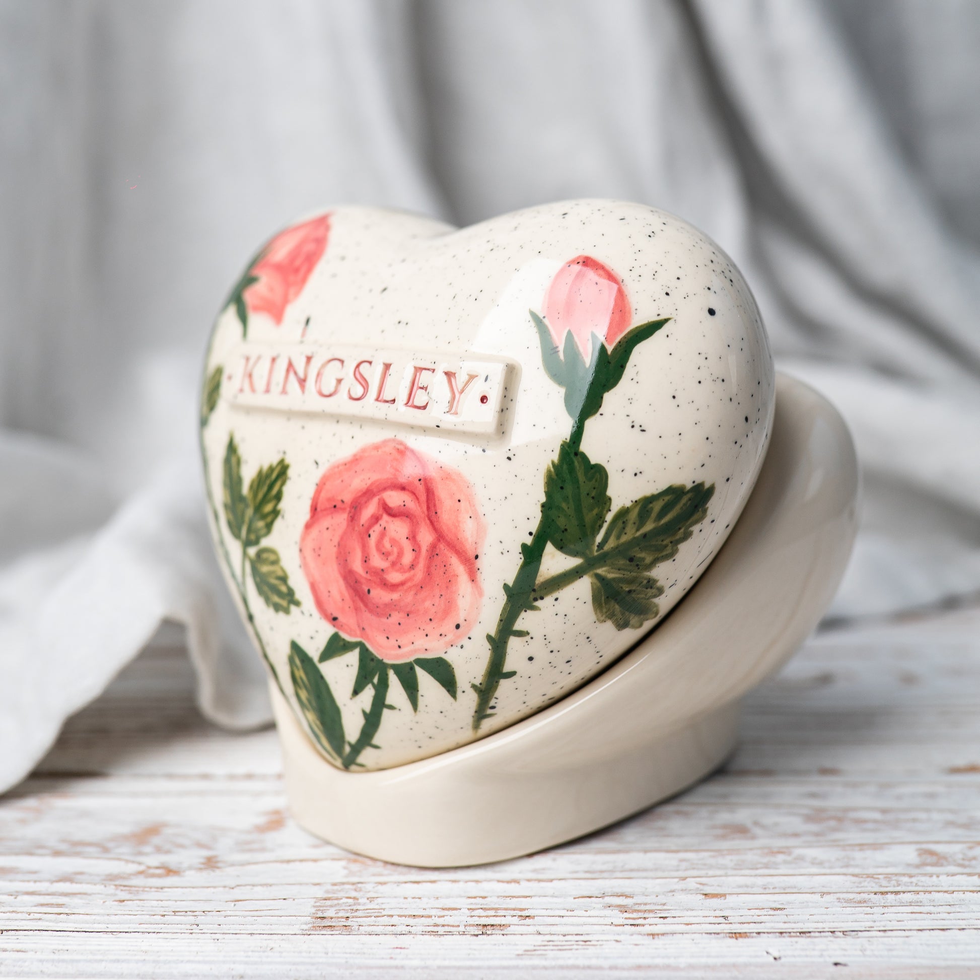 Side profile of the rose memorial urn on its stand, highlighting the smooth glaze and handmade quality.