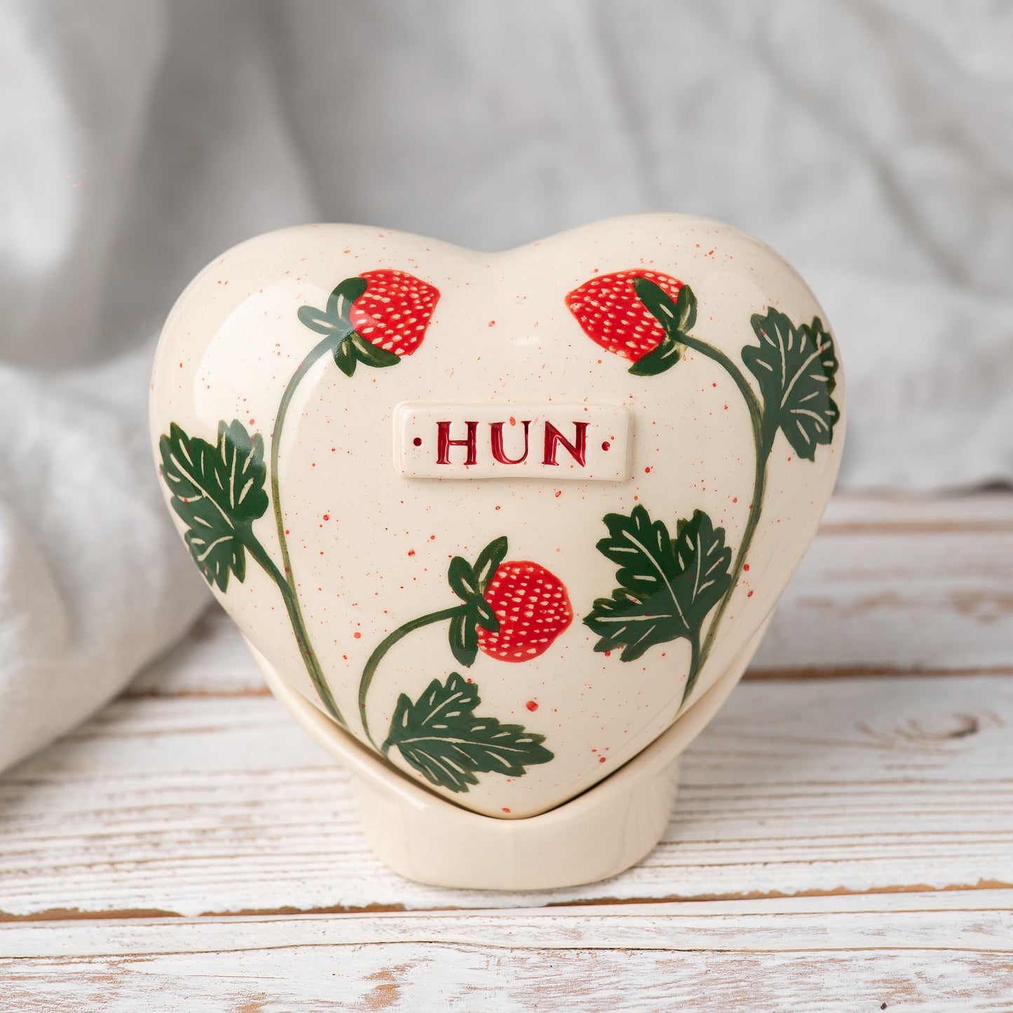 Hand-painted heart-shaped ceramic urn with vibrant strawberries and a matching stand for human or pet ashes.