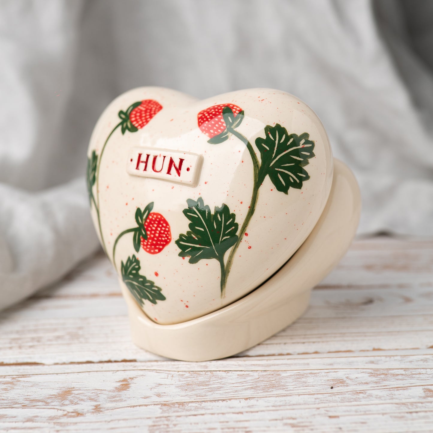 Side profile of the strawberry memorial urn on its stand, highlighting the smooth glaze and artisan pottery quality.