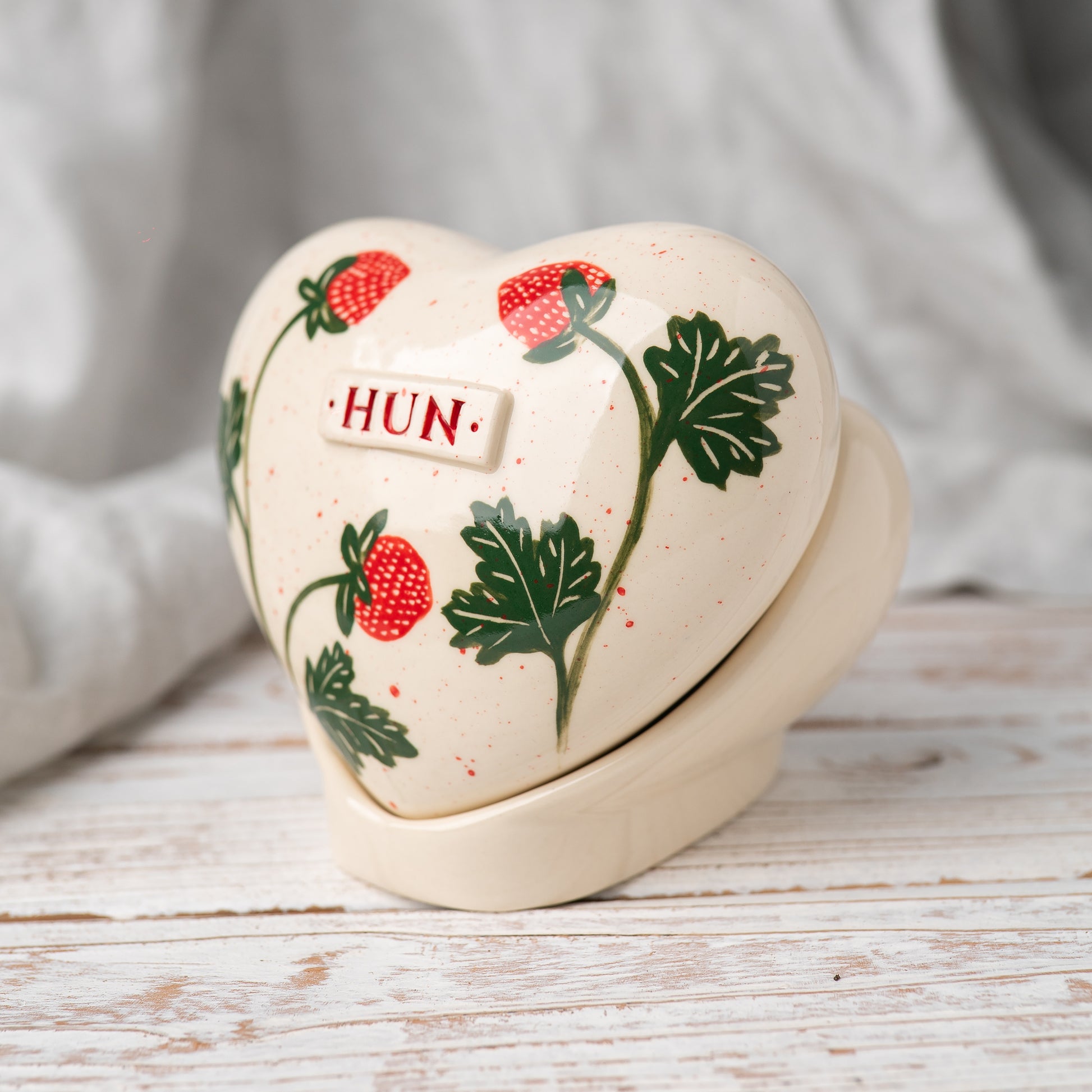 Side profile of the strawberry memorial urn on its stand, highlighting the smooth glaze and artisan pottery quality.