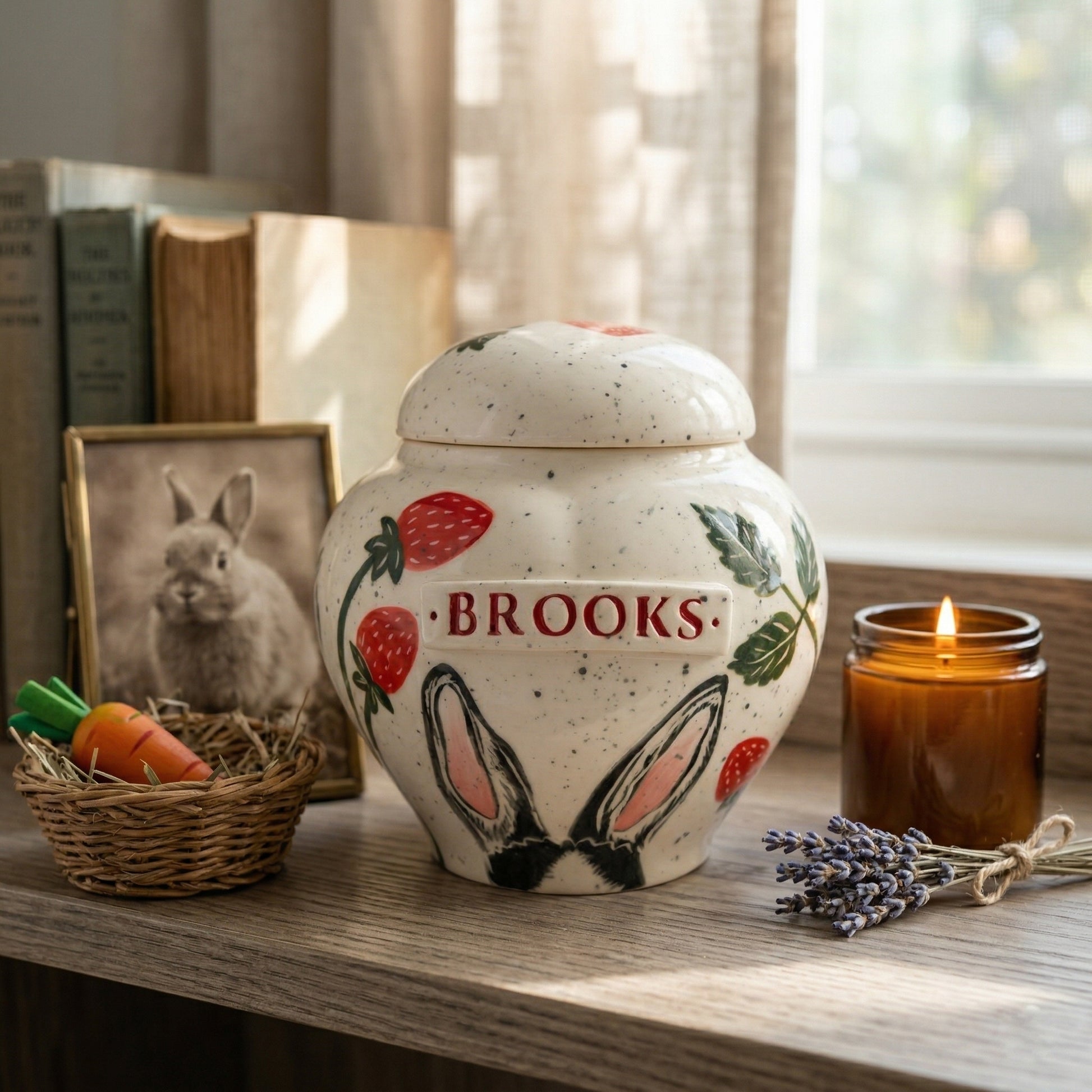 A heartwarming, cozy domestic memory corner display dedicated to a beloved rabbit. Centered on a rustic weathered ash wood shelf is the hand-painted ceramic heart-shaped pot-style urn featuring a naive botany strawberry pattern and delicate painted bunny ears directly on the body