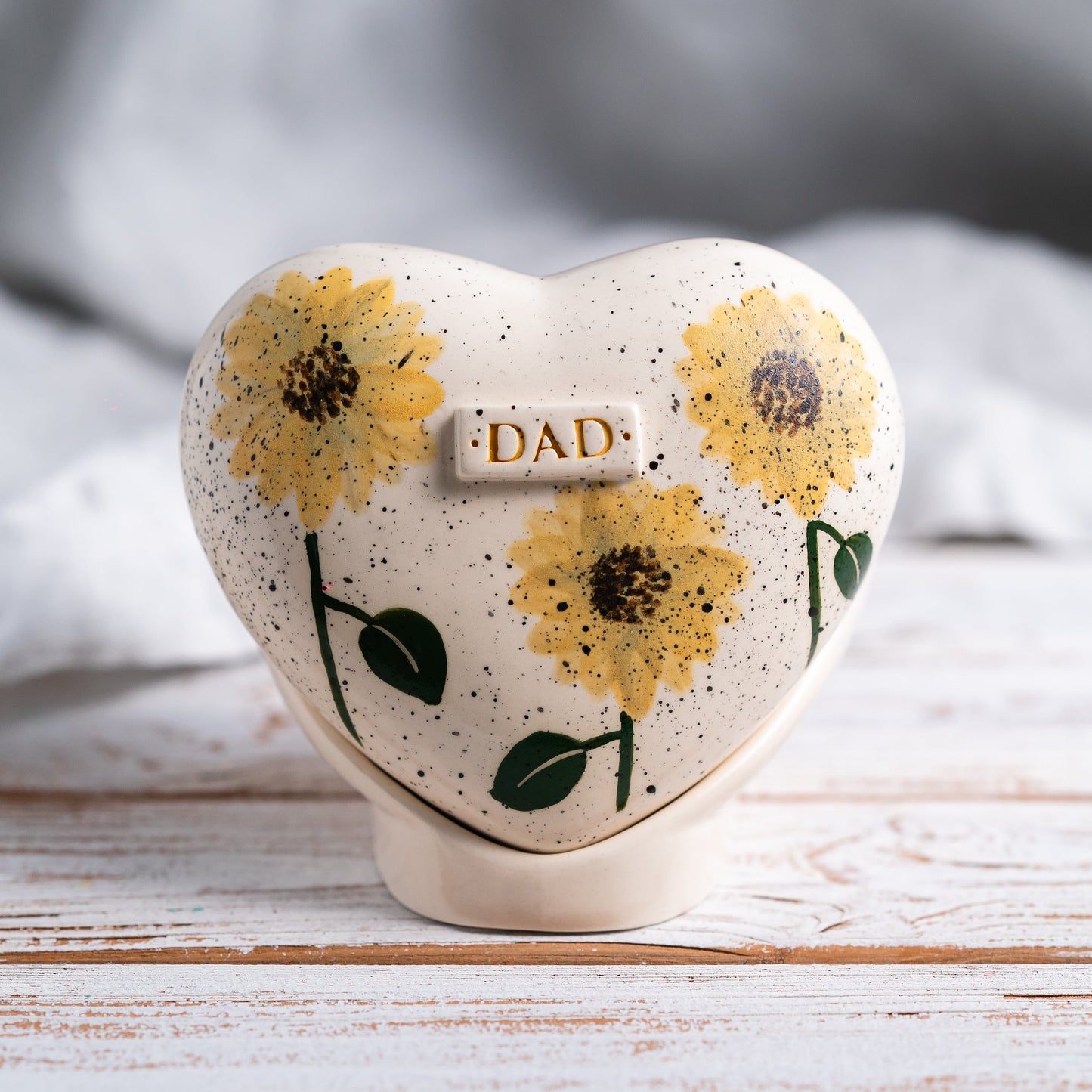 Hand-painted heart-shaped ceramic urn with bright sunflowers and a matching stand for human or pet ashes.