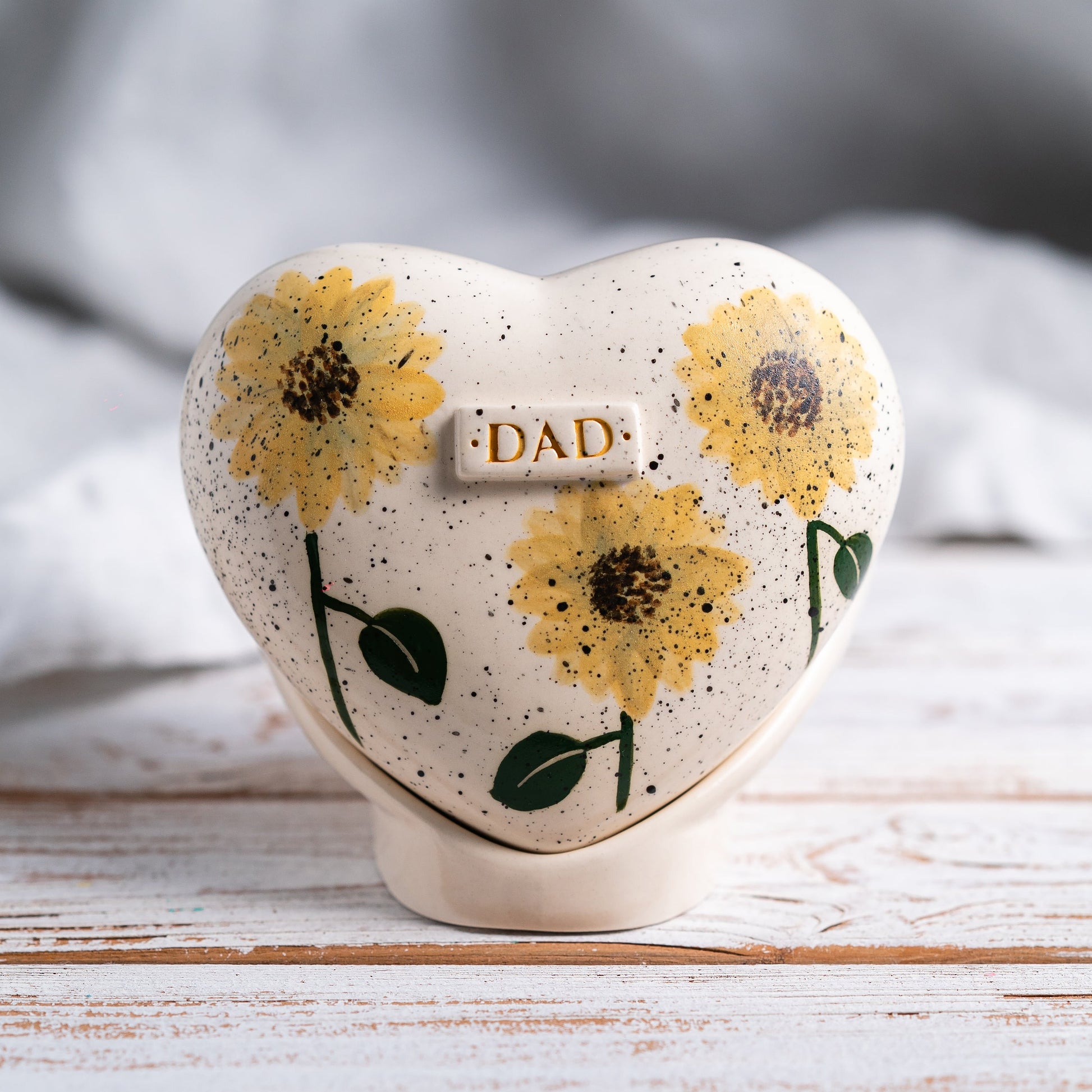 Hand-painted heart-shaped ceramic urn with bright sunflowers and a matching stand for human or pet ashes.