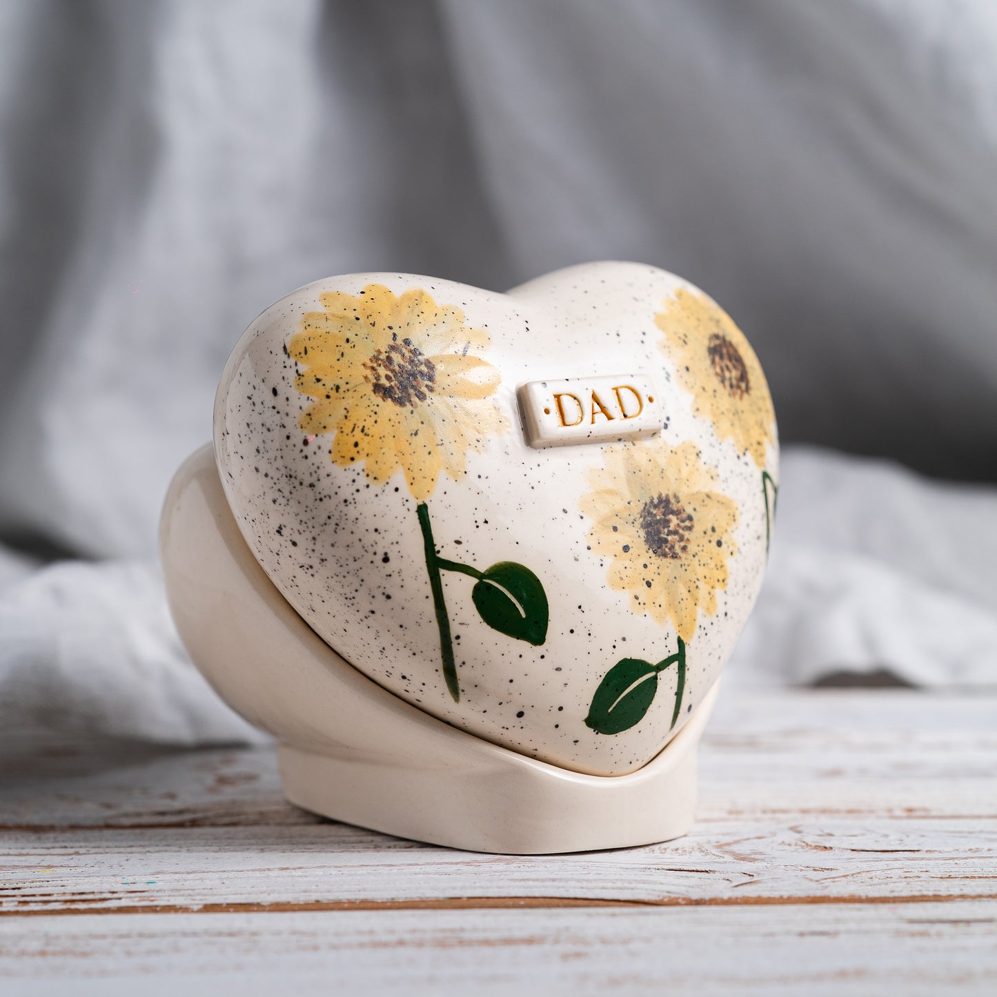 Side profile of the sunflower memorial urn on its stand, highlighting the smooth glaze and handmade quality.