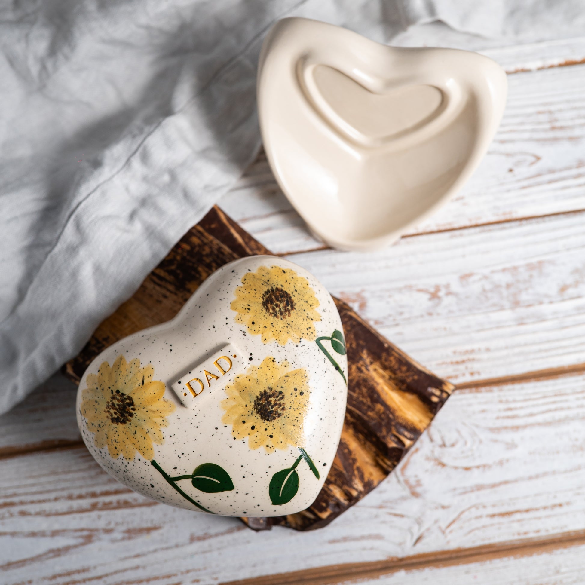 Top view of the ceramic heart urn, showing the detailed yellow sunflower petals and dark center illustration.