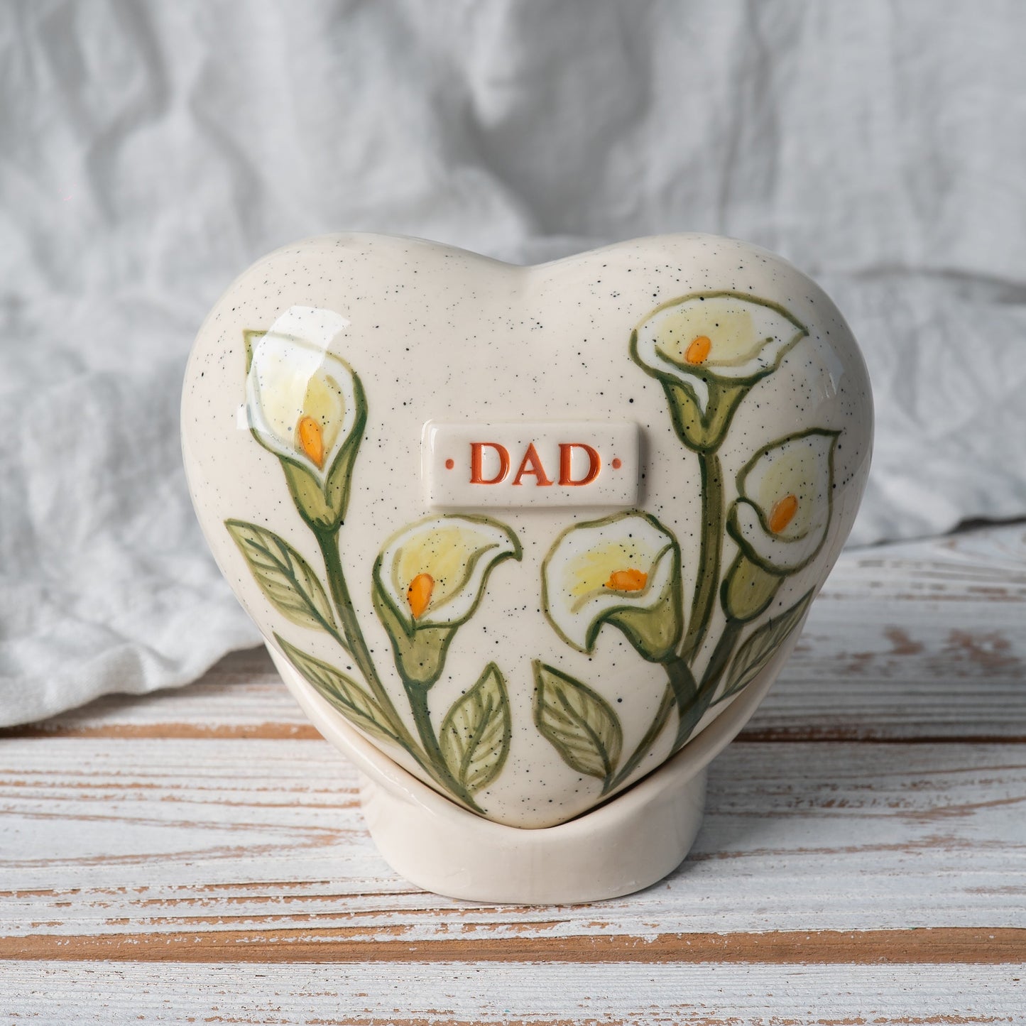 Hand-painted heart-shaped ceramic urn featuring elegant white calla lilies and green leaves on a matching stand by Mira Ceramics