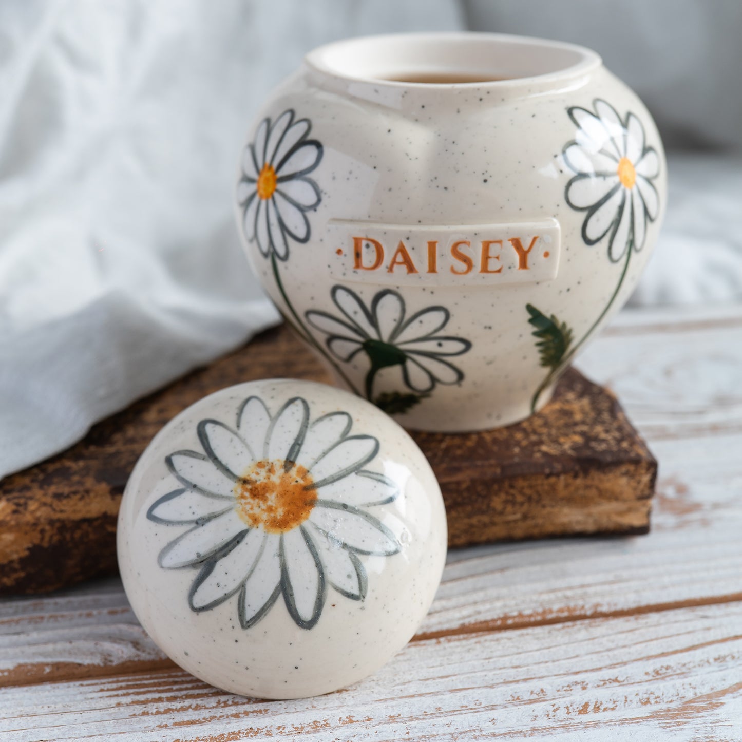 Hand-painted heart-shaped ceramic memorial urn with white daisies in naive botany style with open lid