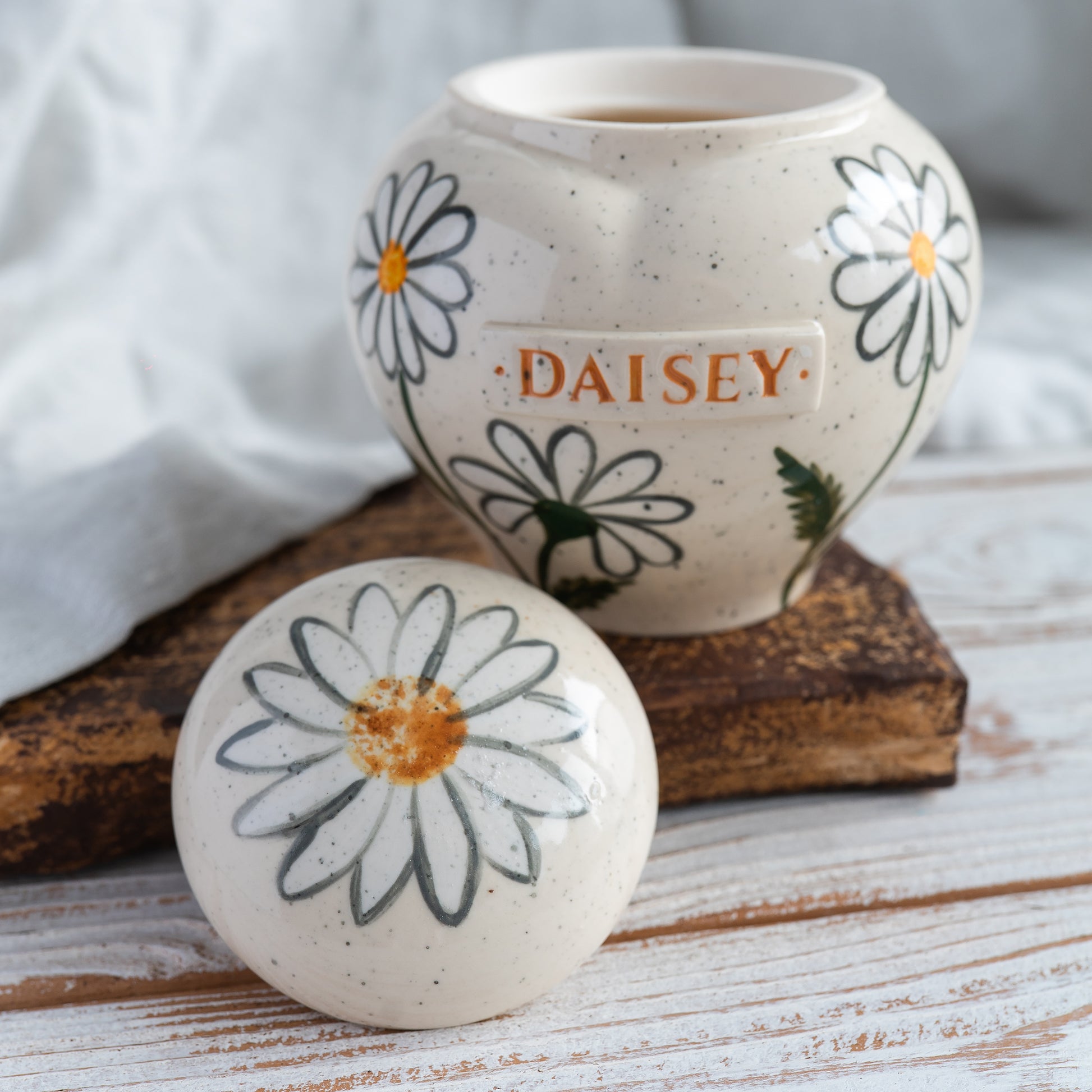 Hand-painted heart-shaped ceramic memorial urn with white daisies in naive botany style with open lid