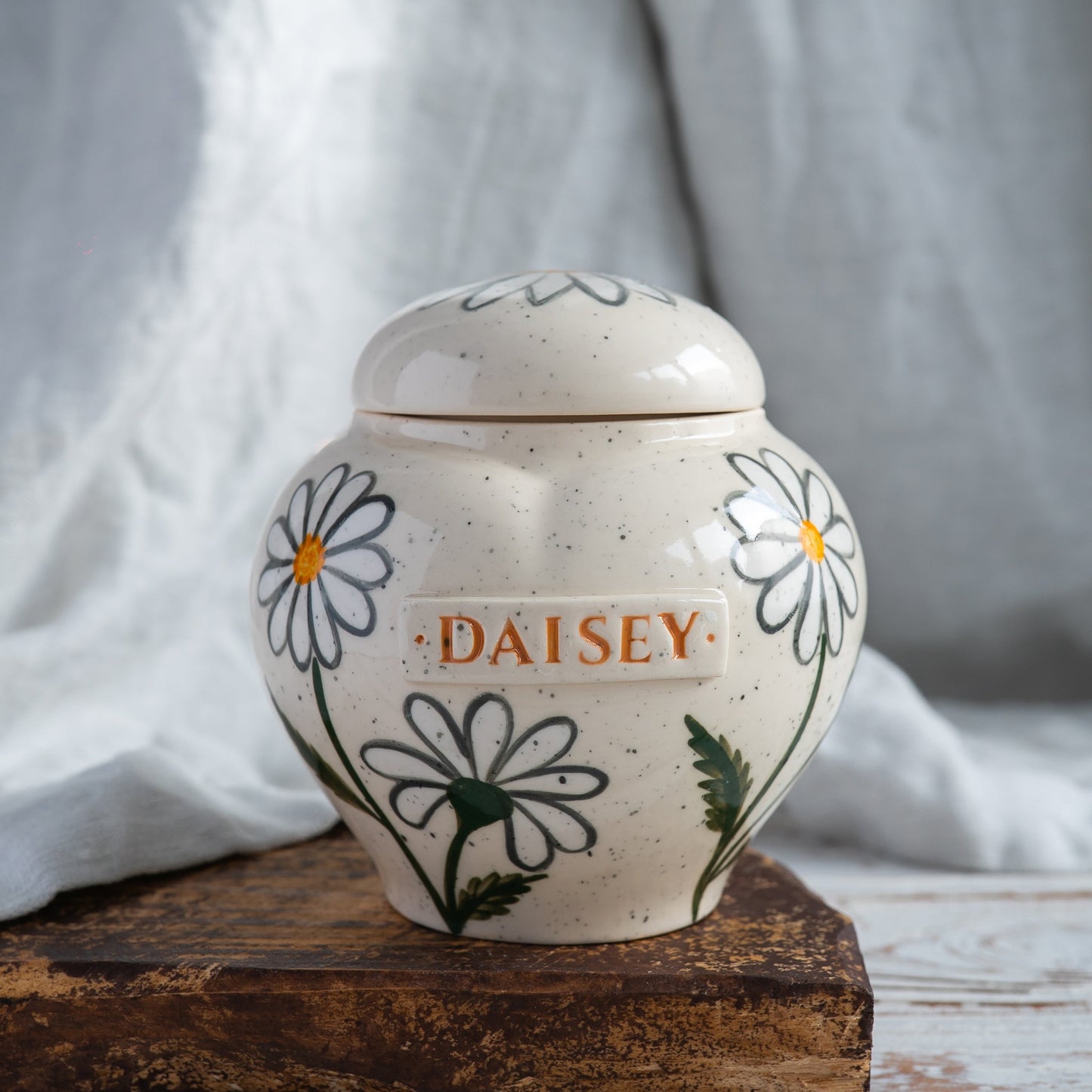 Hand-painted heart-shaped ceramic memorial urn with white daisies in naive botany style.