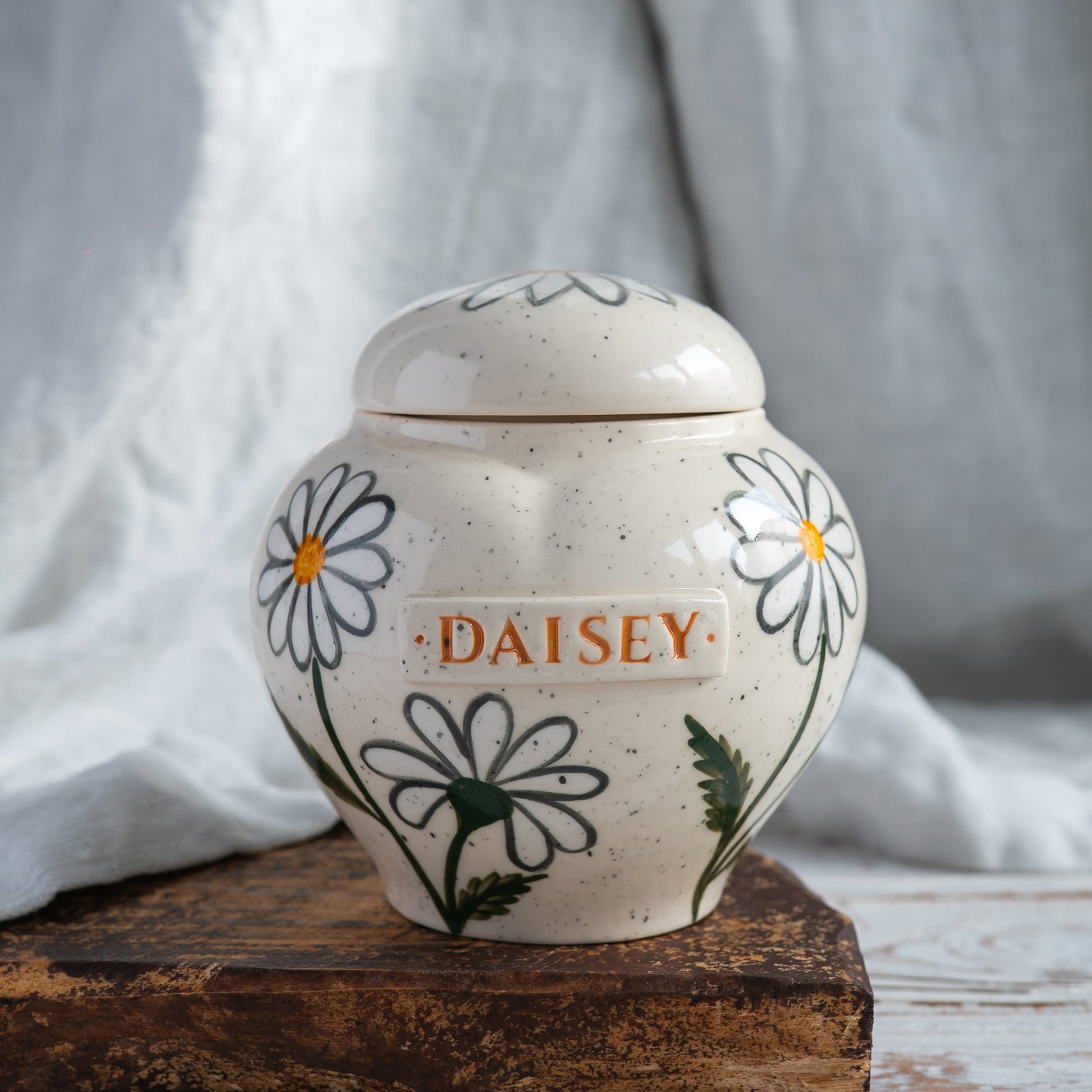 Hand-painted heart-shaped ceramic memorial urn with white daisies in naive botany style.