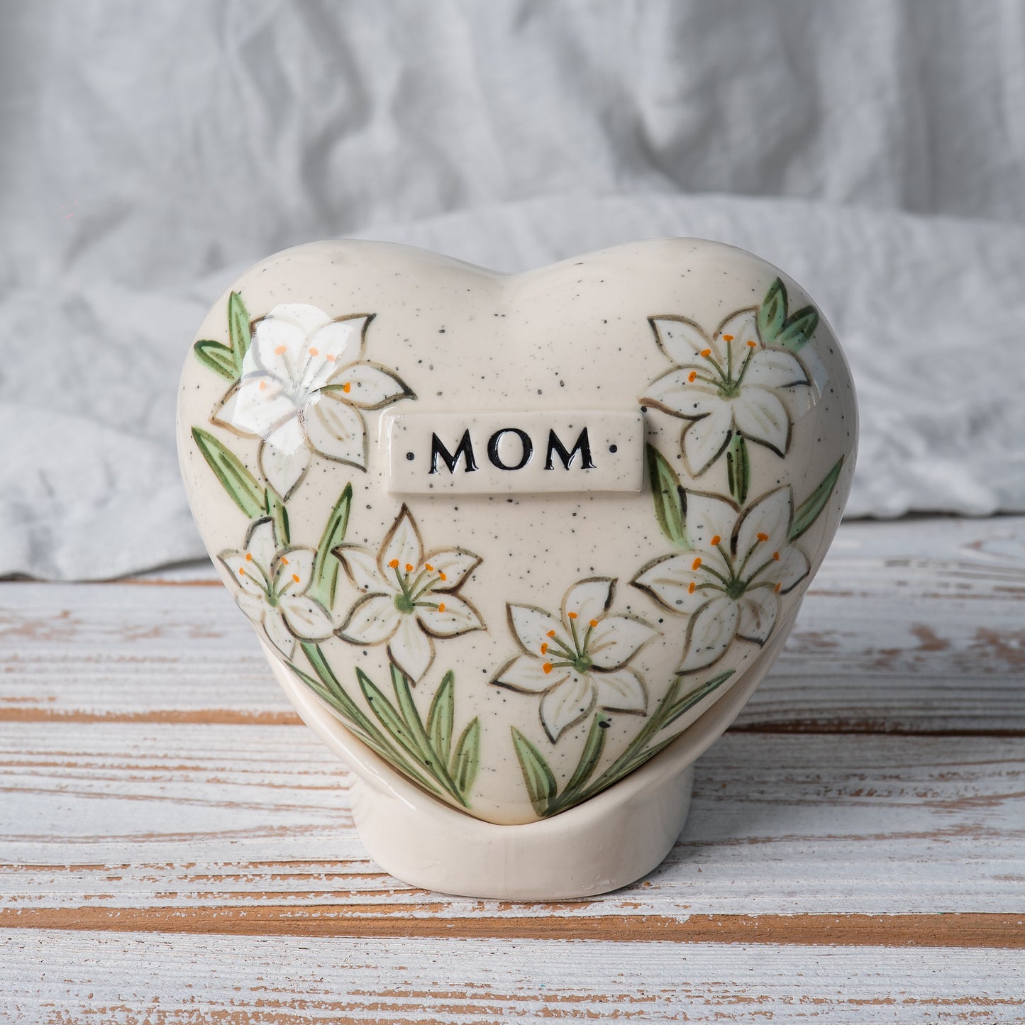 Hand-painted heart-shaped ceramic urn with elegant white lilies and matching stand for human or pet ashes.