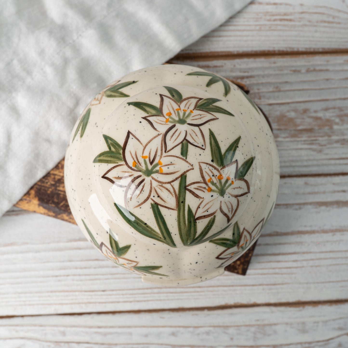 Top-down view of hand-painted ceramic lid with white lily design for heart keepsake urn