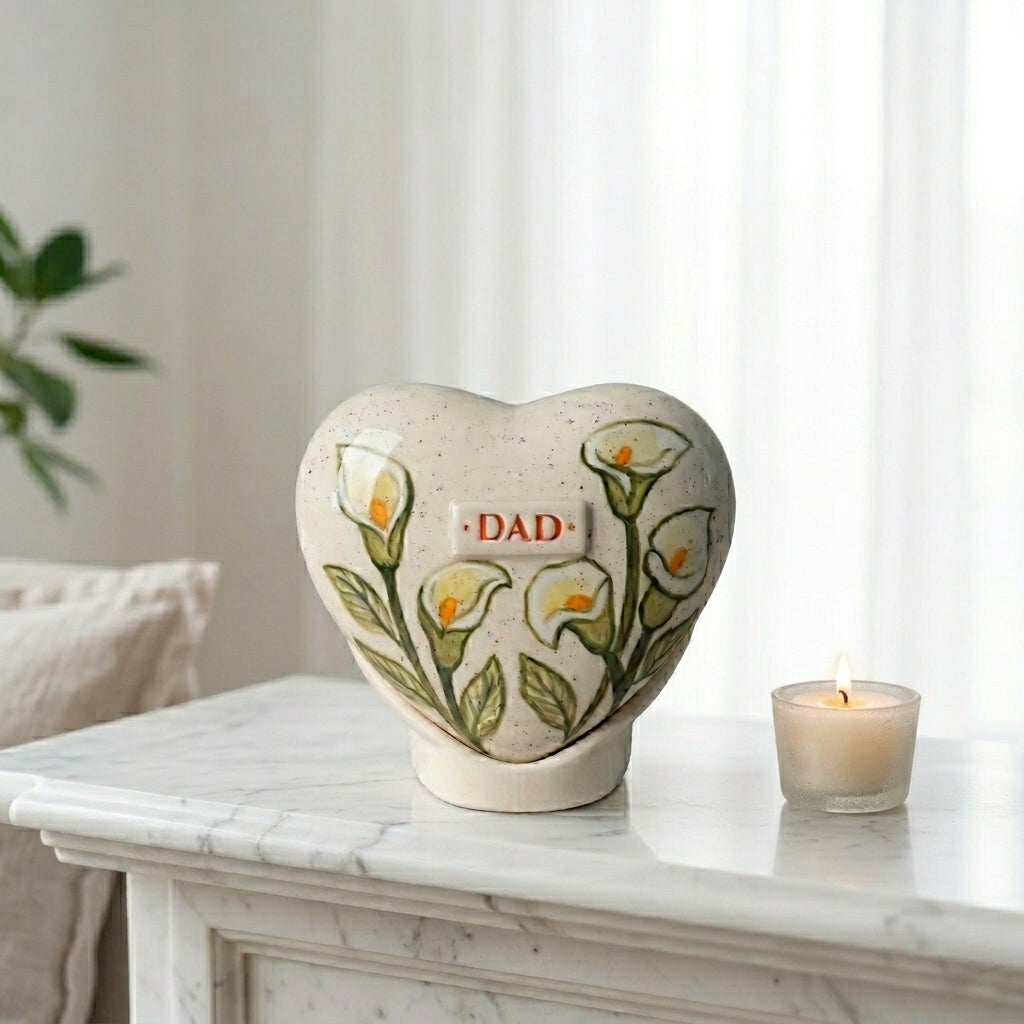 A peaceful memorial display in a bright home interior, featuring the white calla lily heart urn next to a candle