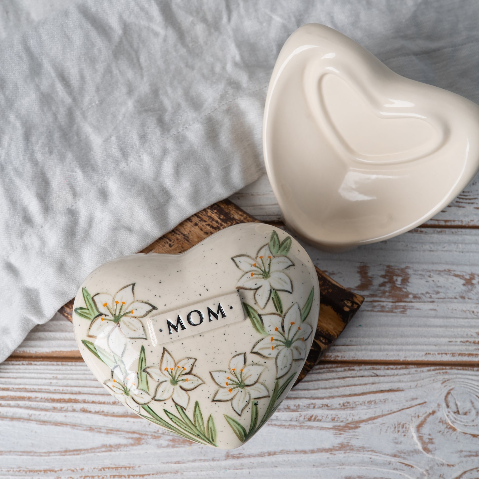 Top view of the ceramic heart urn, showing the detailed white lily petals and botanical leaf design.