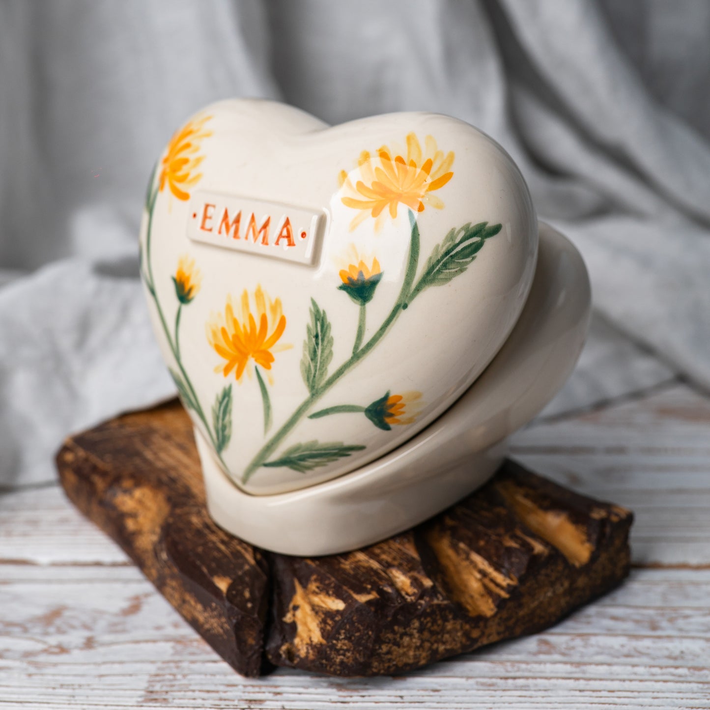 Side profile of the yellow chrysanthemum memorial urn on its stand, highlighting the smooth glaze and handmade quality.