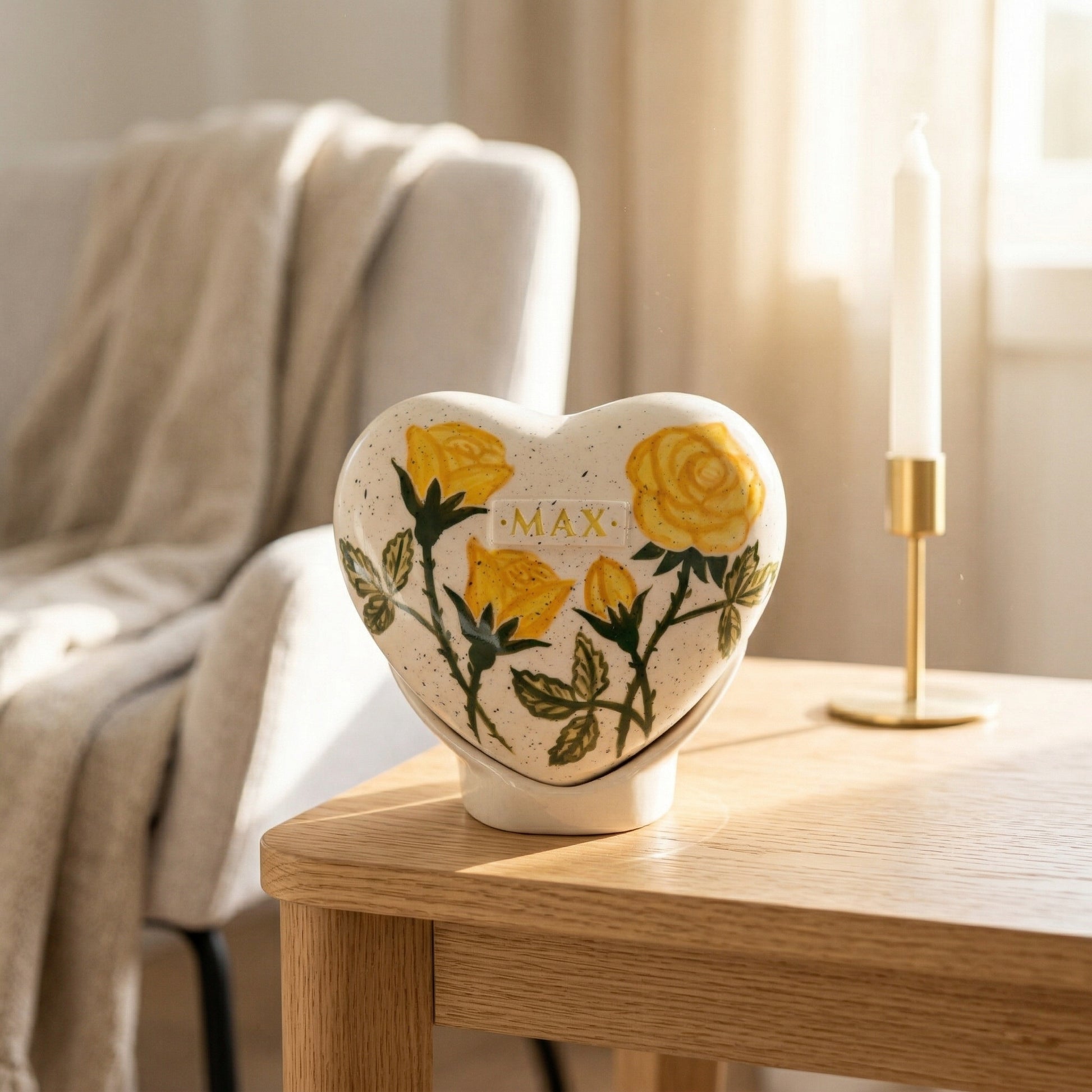 A warm home memorial display with a yellow rose heart urn on a white shelf next to a small candle.